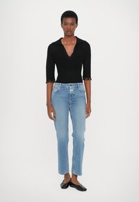 Top negro de manga larga con escote en V profundo y detalles de flecos; jeans de tiro alto y pierna recta de lavado claro; zapatos planos negros. Conjunto sencillo y casual.