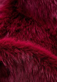 Tissu en fausse fourrure douce et moelleuse de couleur rouge profond, avec des fibres longues et fines densément superposées pour créer une texture pelucheuse.