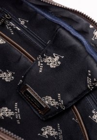 Interno di una borsa con tessuto blu navy caratterizzato da un motivo ripetitivo di giocatori di polo bianchi, e un tirante della cerniera in pelle marrone con dettagli coordinati.