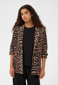 Blazer con stampa leopardata in marrone e nero, con apertura frontale, maniche arrotolate e texture liscia, indossato sopra una camicia nera.