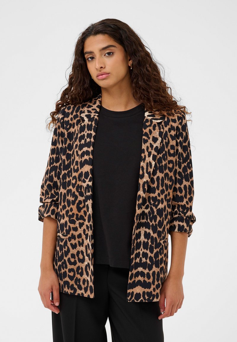 Blazer con stampa leopardata in marrone e nero, con apertura frontale, maniche arrotolate e texture liscia, indossato sopra una camicia nera.