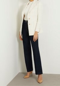 Biały, fakturowany żakiet z złotymi guzikami, połączony z ciemnoniebieskimi spodniami o wysokim stanie i cielistymi szpilkami w szpic.