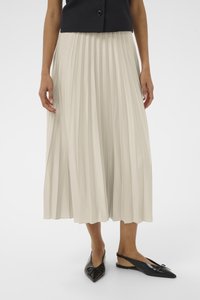 Gonna midi plissettata in tessuto beige chiaro, abbinata a scarpe slingback in pelle lucida nera con un dettaglio a fiocco e punta affusolata.