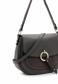 Sac à épaule en cuir marron foncé avec une poche avant en daim, un anneau doré décoratif et une bandoulière réglable avec des clous en métal.