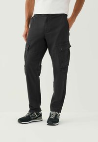 Black cargo pants with a relaxed fit, featuring multiple side pockets and a drawstring waistband. Worn with black sneakers.