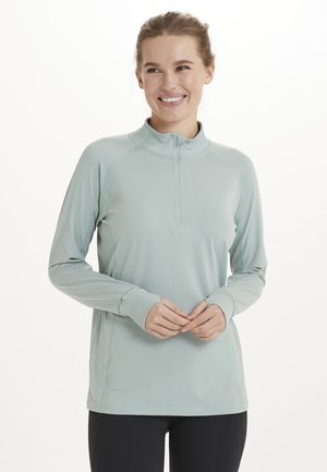 Lyse teal pullover med halv-zip detalje, lange ærmer og flade sømme for en glat pasform. Fremstillet af letvægts, hurtigtørrende materiale.