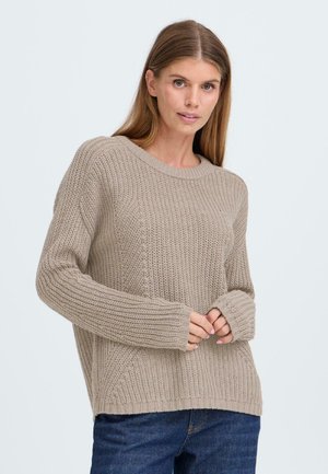 Hellbeige Strickpullover mit strukturiertem Muster, Rundhalsausschnitt und gerippten Bündchen. Kombiniert mit dunklen Jeans.