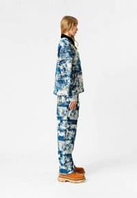 Conjunto de tela de patrón azul y crema que incluye una chaqueta con cuello y pantalones a juego, usado con zapatos beige de suela gruesa.