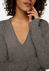 Pull en maille gris avec un décolleté en V profond et des manches longues, offrant une texture douce et une coupe décontractée. Recouvrement total du corps avec un minimum de détails.