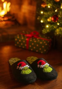 Black fleece slippers featuring a green Grinch design with a red Santa hat. The inner sole is green with heart patterns.