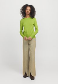 Maglione verde a maniche lunghe abbinato a jeans beige a gamba larga con fessure frontali e stivali alla caviglia marroni. Design in tessuto semplice e testurizzato.