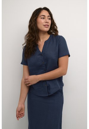Chemise en lin bleu marine à boutons, avec un col en V, des manches courtes et une coupe décontractée. Présente des boutons marron et un ourlet droit.