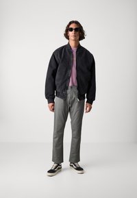 Črn denim bomber jakna preko roza majice, v kombinaciji z olivno zelenimi hlačami in črnimi supergami z belimi podplati. Kodrasta pričeska in sončna očala.