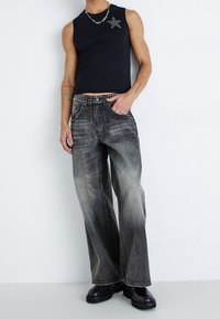 Svart ärmlös topp med en rhinestones-design av en stjärna, kombinerad med grå vida jeans med en slitning och nitar på bältet.