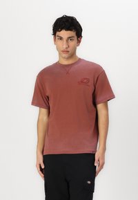 Tricou din bumbac maro, cu gât rotund, mâneci scurte și un logo mic. Prezintă o cusătură simplă și o croială lejeră.
