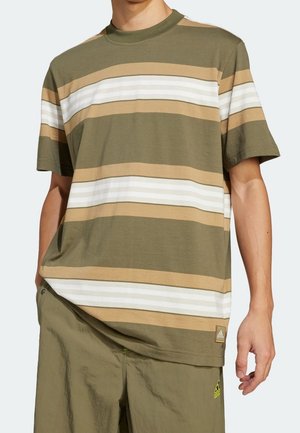 Man draagt een T-shirt met korte mouwen in olijfgroen, beige en wit gestreept, en olijfgroene broek, staat met zijn rechterhand ontspannen langs zijn zij.