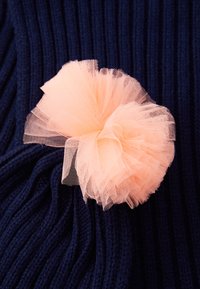 Tissu en tulle rose clair rassemblé en une forme de nœud duveteux sur un fond de tissu tricoté noir bleu foncé.