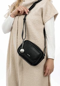 Borsa a tracolla nera in pelle con dettagli intrecciati, hardware argentato e tracolla staccabile, appoggiata contro un capo esterno di colore chiaro e texture.