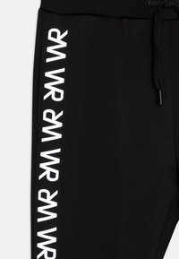 Zwarte sweatpants met een gestructureerde afwerking, voorzien van witte logotekst langs de zijkant en een trekkoord in de taille voor een verstelbare pasvorm.