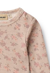 Langärmliges Babyshirt aus weich beigem Stoff mit kleinem rosa und lila Blumenmuster, ausgestattet mit Druckknöpfen an den Schultern für ein einfaches Ankleiden.