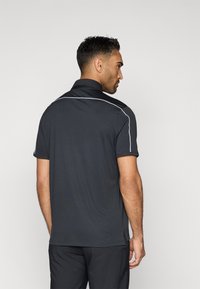 Polo noir avec un tissu texturé, présentant des lignes d'accent blanches le long des épaules et des coutures latérales. Manches courtes et col classique.