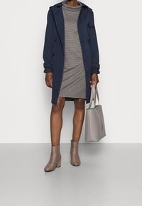 Námořnický trenčkot s černými knoflíky, šedé žebrované šaty, taupe kotníkové boty a světle šedá kabelka. Hladká textura a přiléhavý design.