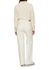 Camisa blanca de manga larga combinada con pantalones sueltos de color crema. Incluye un cuello con botones y un diseño recto con bolsillos traseros.