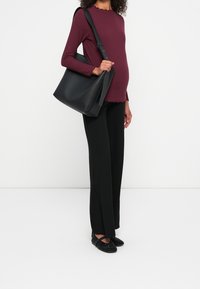 Vinröd ribbad tröja med vågig nederkant, svarta vida byxor och svart tote-väska. Skorna består av texturerade svarta Ballerinaskor med dekorationer.