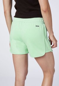 Světlé zelené sportovní šortky vyrobené z měkké tkaniny, s elastickým pasem a bočními rozparky. Malá logo nášivka na zadní straně.
