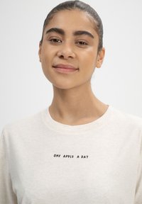Hellbeige Sweatshirt mit Rundhalsausschnitt, mit dem Text "EINEN APFEL PRO TAG" in Schwarz. Weiche Stoffstruktur, lässiges Design.