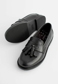Mocassins en cuir noir avec une finition lisse, dotés d'un accent en frange et en gland. Semelle en caoutchouc noir texturée pour une meilleure adhérence. Doublure ornée de motifs en forme de cœur.