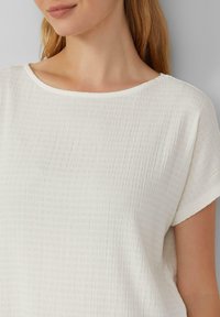 Witte, textuurstof top met een ronde halslijn en korte mouwen. Bevat subtiele verticale plooien voor extra visuele interesse.