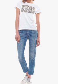 Camiseta blanca con un patrón gráfico rectangular en blanco y negro, combinada con unos pantalones vaqueros de mezclilla ligeros y zapatillas grises.