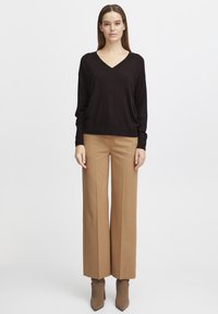 Schwarzer V-Ausschnitt-Pullover mit langen Ärmeln, kombiniert mit hoch taillierten, weiten beigen Hosen und passenden hochhackigen Stiefeletten.
