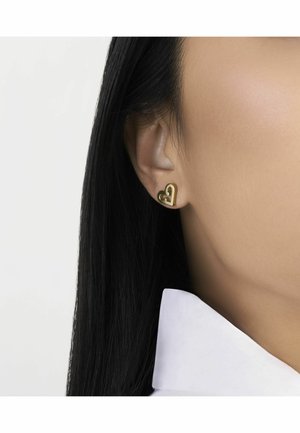 Boucles d'oreilles pendantes en forme de cœur doré présentées sur l'oreille d'un modèle, avec une finition lisse et un design minimaliste.