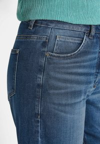 Jean en denim bleu à coupe droite, avec un design classique à cinq poches et de subtils détails de couture. Tissu texturé, lavage moyen.