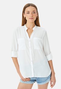 Witte lange mouwen knoopshirt met een staande kraag, twee frontzakken en opgerolde manchetten, gemaakt van een gladde stof. Casual ontwerp.