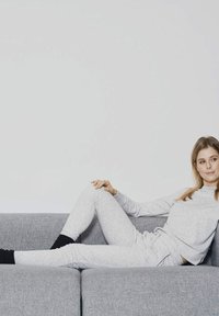 Conjunto de loungewear texturizado en gris claro, con una camiseta de cuello redondo y pantalones ajustados, que presenta puños de canalé negros, usado mientras se está reclinado en un sofá gris.