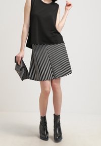 Svart ärmlös topp kombinerad med en utsvängd kjol med svart och vitt diagonalt randmönster. Modellen håller en svart kuvertväska och har på sig svarta ankelstövlar.