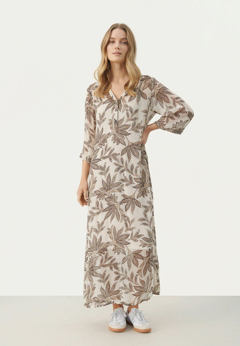 Robe maxi à manches longues, motif floral marron et beige, décolleté en V, taille cintrée, associée à des baskets blanches, en tissu léger.