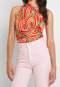 Haut halter haut en couleur avec des motifs tourbillonnants rouges, oranges et verts, associé à un jean taille haute rose clair. Texture de tissu lisse.