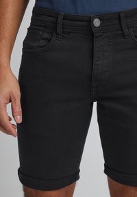 Black denim shorts with a slim fit, featuring rolled hems, five pockets, and a button waist closure. Smooth texture and versatile design.