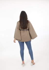 Beige översized topp med vida ärmar, knuten i midjan med ett svart bälte. Kombineras med blå skinny jeans och klara klacksandaler.