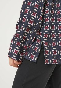 Langärmliges Hemd aus marineblauem Stoff mit einem geometrischen Muster aus roten Sternen und cremefarbenen Akzenten, mit knöpfbarem Manschette und seitlichen Schlitzen.
