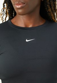 Svart treningsgenser med rund hals, laget av et glatt, elastisk materiale. Har en hvit Nike-logo på brystet.