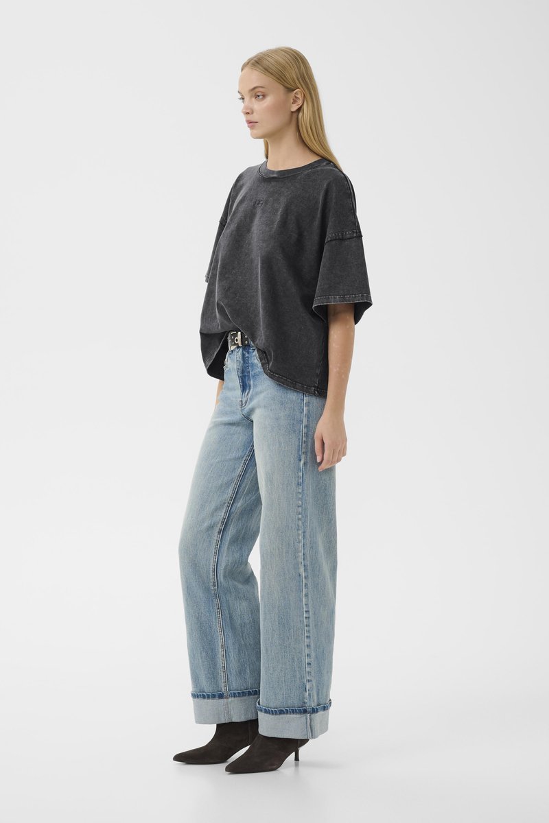 Overdimensioneret sort bomulds-t-shirt med drop-skuldrer, parret med lyseblå højtaljede jeans med en frynset kant og sorte hæle.