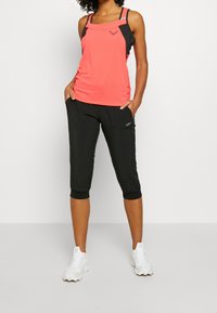 Top sin mangas color coral con detalles en negro, combinado con pantalones capri negros que presentan un logo, ambos confeccionados con una tela ligera y transpirable.