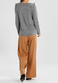 Szary, długi rękaw z marszczonymi akcentami na ramionach, w połączeniu z luźnymi, beżowymi spodniami o szerokich nogawkach i czarnymi butami na obcasie.