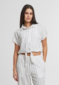 Camicia a maniche corte a righe bianche e nere con un nodo sul davanti, abbinata a pantaloni larghi in tessuto testurizzato.