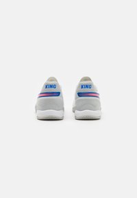 Zapatillas deportivas grises con un acabado texturizado, que presentan un logo azul "KING" y una franja de acento rosa en los lados. Material suave y flexible.